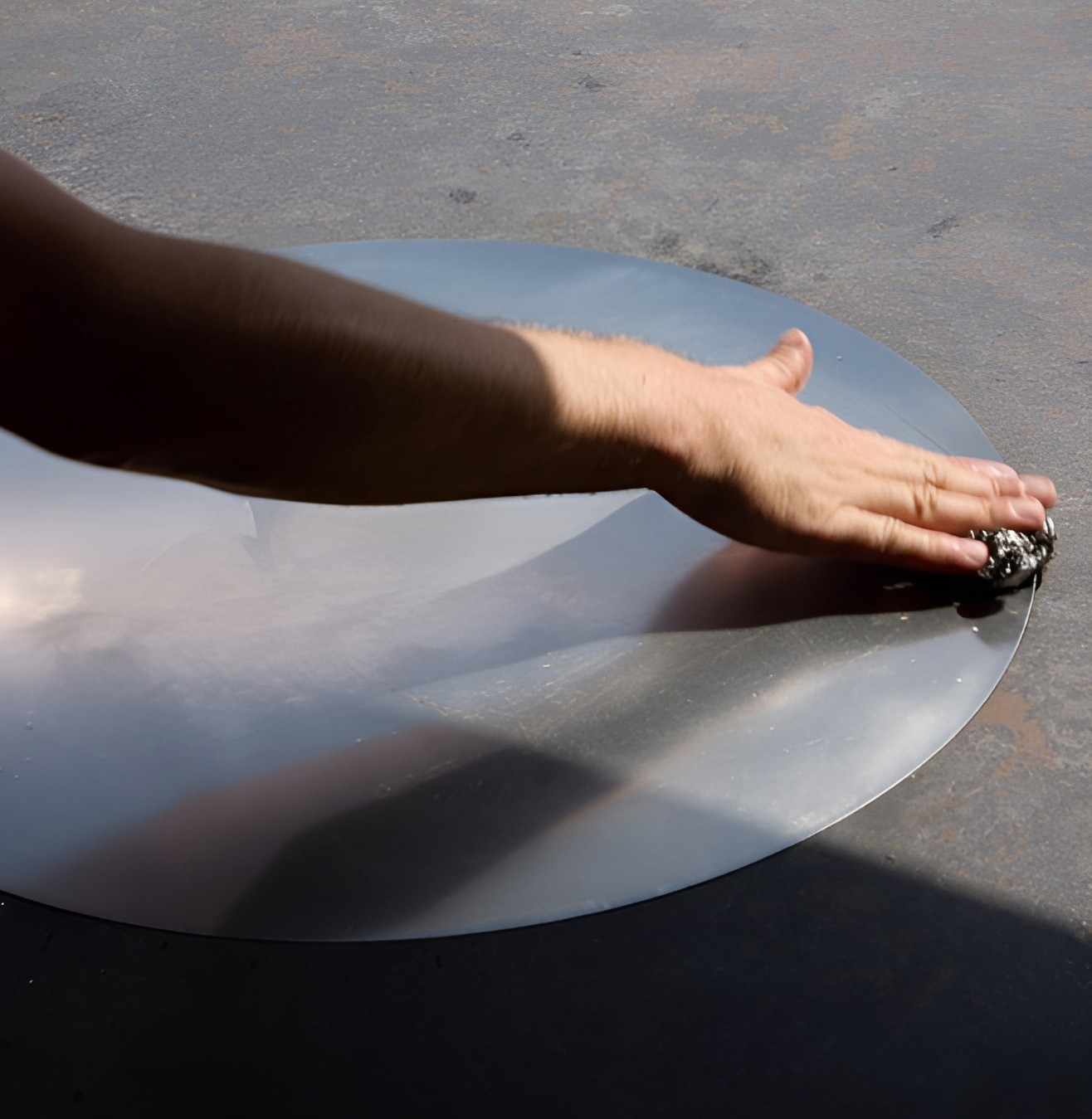 Eine Hand wischt eine runde Grillfläche sauber.